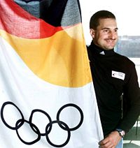Der Rennrodler Georg Hackl am Frankfurter Flughafen vor seiner Abreise nach Salt Lake City, neben einer Olympiafahne (3. Februar 2002).
